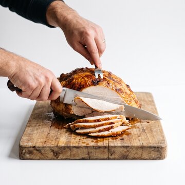 Man carving a golden brown roasted turkey on a wooden cutting board for Thanksgiving dinner celebration