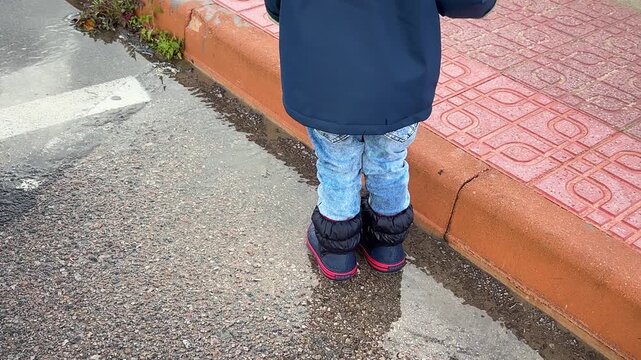 A little boy walks through puddles in rubber boots after the rain. 4k, slow motion.