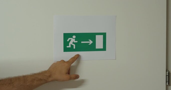 Close-up of a hand pointing at an emergency exit sign. Ideal for workplace safety, evacuation routes, emergency preparedness, and building compliance concepts.