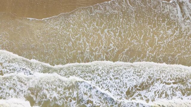 Aerial view from above of breaking waves in parallel lines near sandy shore. Sea foam texture for background use