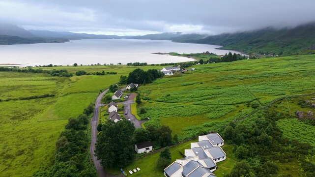 Drone rising over white houses and patchwork croftland toward Loch Torridon and steep Scottish Highland mountains shrouded in low cloud