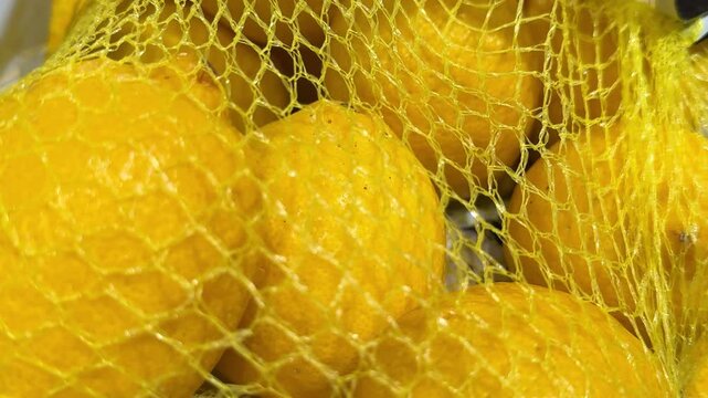 Bright citrus fruit packaged in yellow mesh bags creates a colorful grocery display, offering convenient portions for supermarkets, local markets and everyday shopping. Close up.