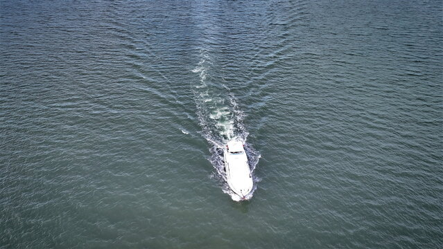 Aerial view of a white boat navigating through calm blue waters, leaving a visible wake behind it in Sabana de la Mar, Hato Mayor Province, Dominican Republic.