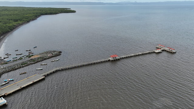 Aerial view of the wooden pier with red-roofed gazebos extending into the sea, with boats near the lush mangrove coastline in Sabana de la Mar, Hato Mayor Province, Dominican Republic.