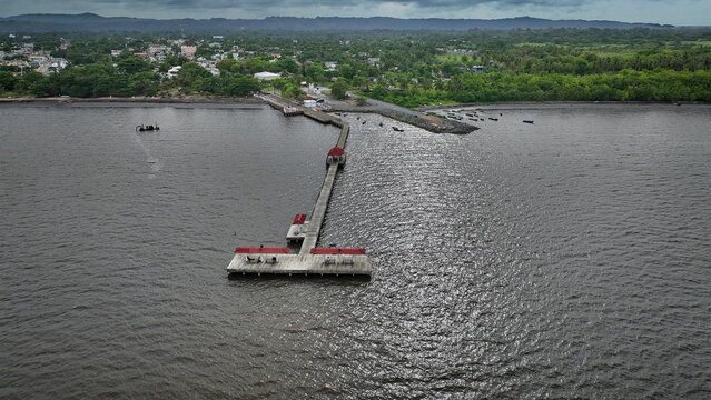 Aerial view of the wooden pier in Sabana de la Mar extending into the bay with red-roofed shelters and lush green coastline, Sabana de la Mar, Hato Mayor Province, Dominican Republic.