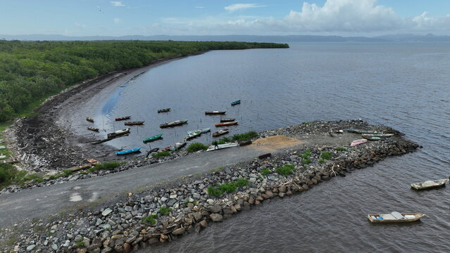 Aerial view of small fishing boats moored near a stone jetty and lush mangroves along the shoreline in Sabana de la Mar, Hato Mayor Province, Dominican Republic.
