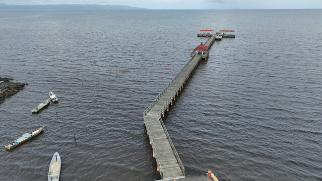 Aerial view of the wooden pier extending into the calm waters of the bay with small fishing boats moored nearby in Sabana de la Mar, Hato Mayor Province, Dominican Republic.
