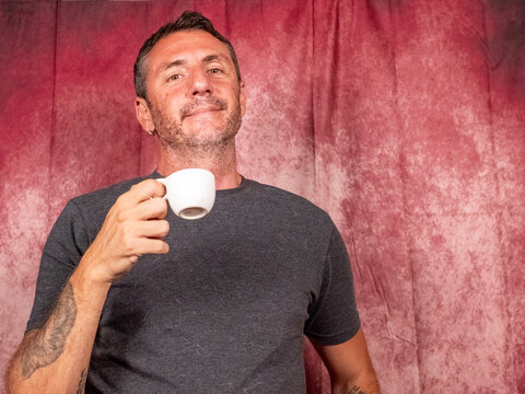 A man drinks an Italian coffee from a small white porcelain cup. The man is forty-two years old, has short hair and a short beard and wears a dark T-shirt