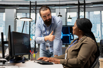 Fototapeta premium Pleased technology company manager gives a female developer a thumbs-up after she optimizes code, providing positive feedback for tasks completed during a workplace performance review.