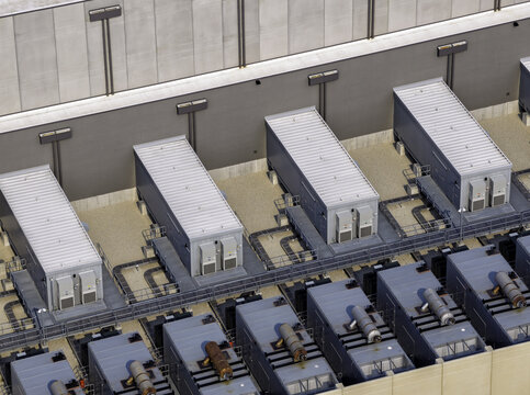 Aerial view of a data center featuring rows of industrial cooling units and power generators on a rooftop, with metal conduits and concrete walls in Illinois, United States.