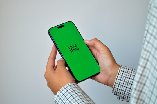 Person holding modern smartphone with Uber Eats food delivery app displayed on bright green screen against neutral gray background