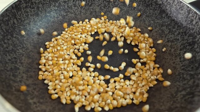 Close-up of yellow corn kernels falling into a frying pan for roasting