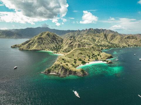Aerial view of Komodo Island featuring lush green hills, white sand beaches, and turquoise waters with boats in the sea, Komodo, East Nusa Tenggara, Indonesia.
