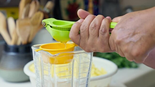 Hands squeezing fresh lime juice using a green manual press into a blender