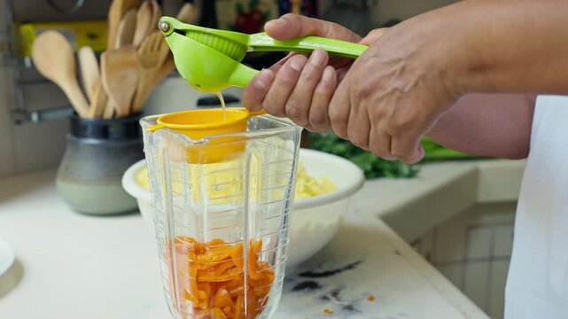 Hands squeezing fresh lime juice using a green manual press into a blender