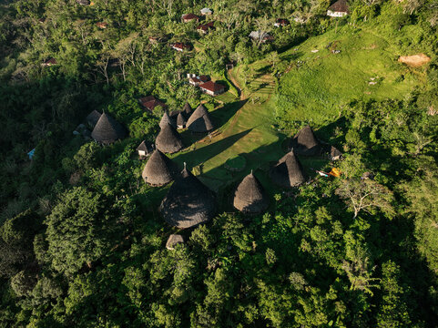 Aerial view of Waerebo Village with its traditional cone-shaped thatched houses situated in a lush green mountain forest in Satar Mese Barat, East Nusa Tenggara, Indonesia.