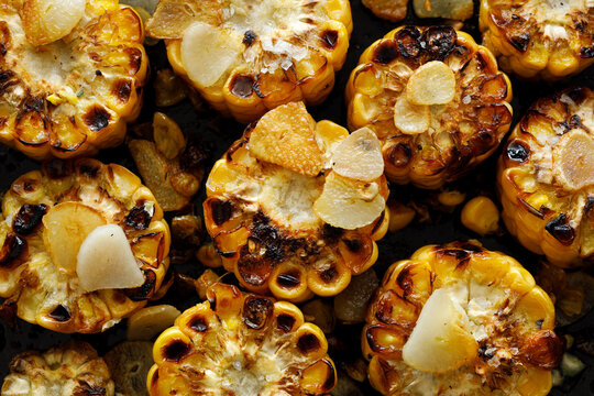 Grilled corn cob rings with addition butter and garlic slices, close-up.