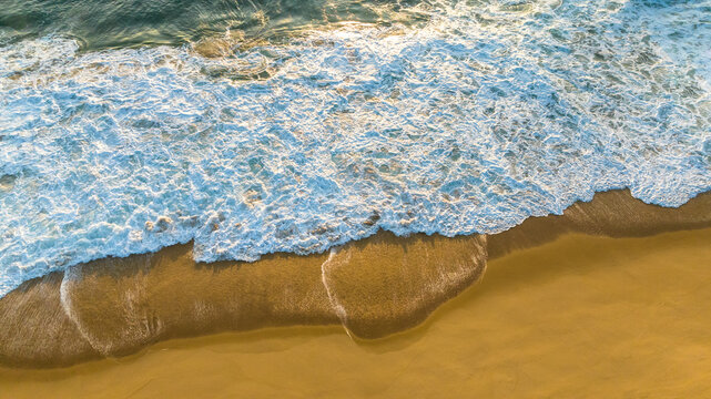 Aerial view of turquoise waves crashing onto the golden sands of Praia das Laranjeiras, Balneario Camboriu, Santa Catarina, Brazil.