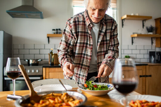 Senior man preparing salad in cozy home kitchen