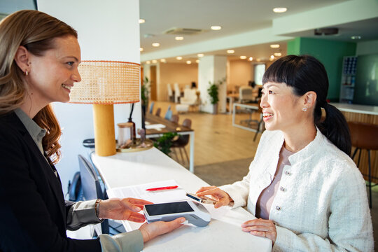 Two women making contactless smartphone payment at modern office reception desk