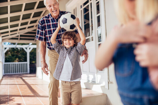Grandfather and boy playing with soccer ball on home porch