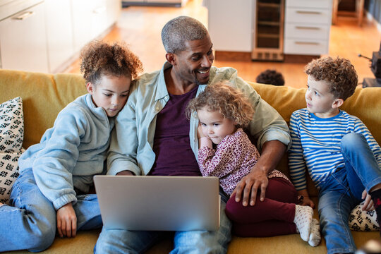 Father and children watching laptop on sofa at home