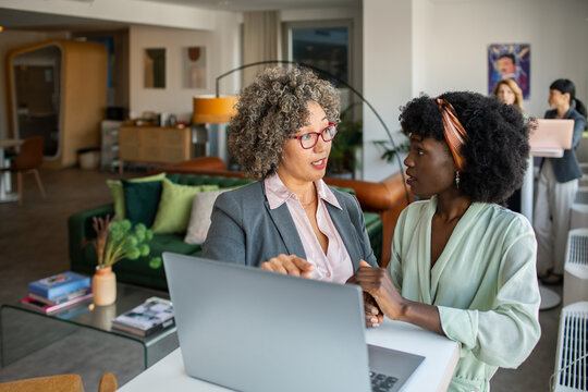 Two businesswomen discussing project at laptop in modern coworking office