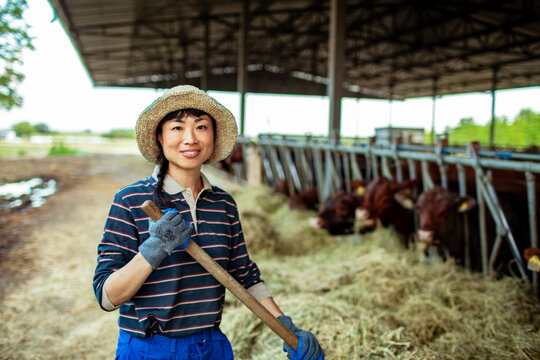 Smiling woman farmer with pitchfork in cattle barn