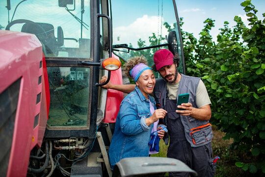 Two farmers checking smartphone beside tractor in orchard
