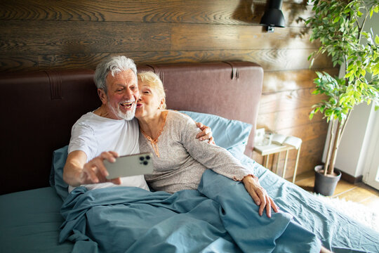 Senior couple taking selfie in bed at home