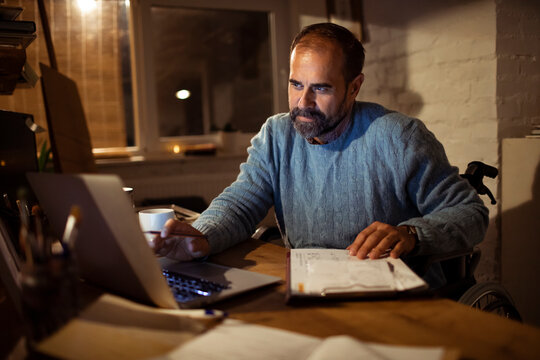 Middle-aged man in wheelchair working late at home office