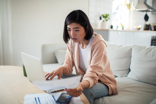 Young woman managing bills on laptop at home