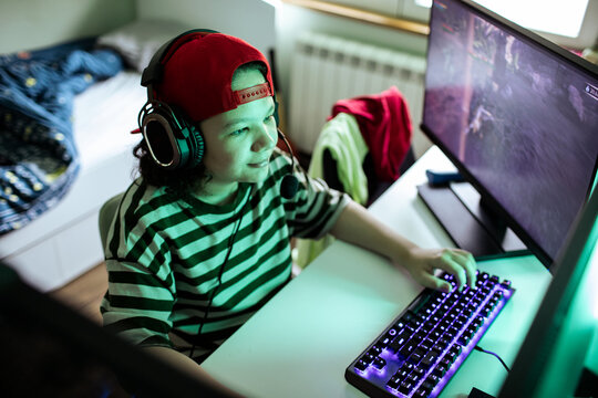 Kid gamer wearing headset playing on computer at home