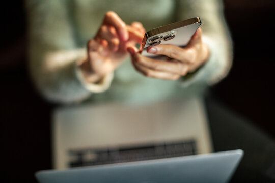 Person using smartphone while working on laptop at home
