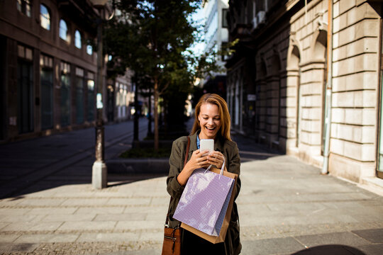 Young woman using smartphone with shopping bags on urban street
