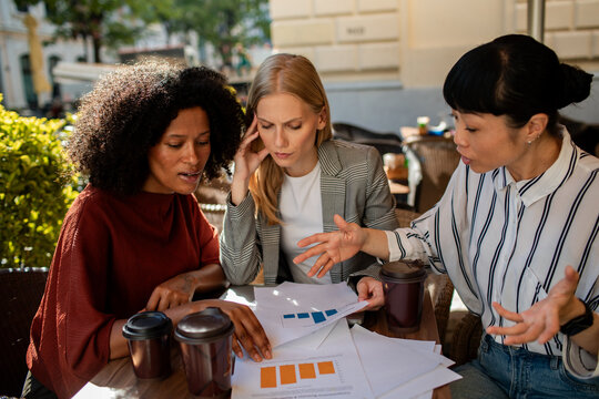 Three businesswomen reviewing charts at outdoor cafe