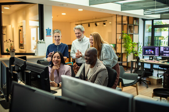 Diverse coworkers celebrating success at computers in modern office