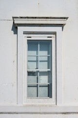 Fototapeta premium Old architectural window in classic colonial style with wood frame, exterior white wall, single-hung sash with grids 