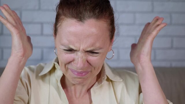 Stressed woman inserting earplugs for noise protection. Unhappy middle-aged woman suffering from a headache due to loud noise, covering her ears and then inserting earplugs, finally feeling relief