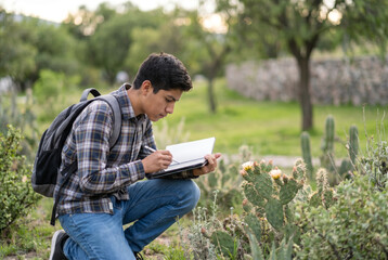 Fototapeta premium Student Observing Nature in the Park. A Latino high school student observing native plants in a green park for a biology project 