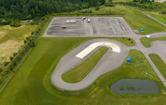 Aerial view of a driving training track with a U-shaped course and a parking area with trucks surrounded by green fields in Vilnius, Vilniaus apskritis, Lithuania.