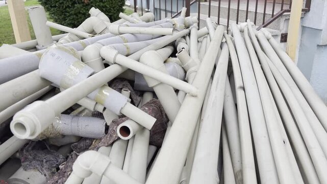 A pile of disassembled plastic water pipes with foam thermal insulation lies stacked outdoors. These plumbing materials are collected and prepared for waste management
