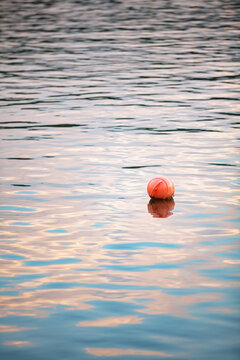Pink marker buoy floating on calm water with pastel sunset reflections