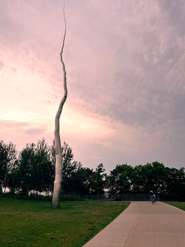 Low angle view showing tall spiraling silver metal One Hindred Foot Line  sculpture resembling lightning bolt at Kiweki Point park at sunset, June 2026