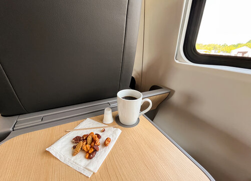 Coffee mug and pile of mixed nuts on napkin on train business class tray table 