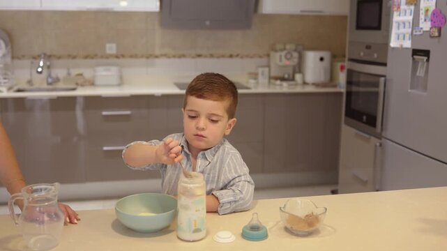 Little boy preparing baby bottle formula at kitchen counter
