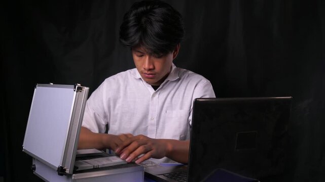 Dishonest employee packs a silver briefcase full of cash and hastily runs away from his laptop. Concept of embezzlement, corporate theft, absconding with funds, and financial crime.
