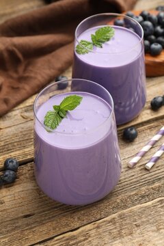 Tasty blueberry smoothie in glasses, fresh berries and mint on wooden table, closeup