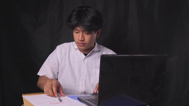 Young man at a desk reviews a rejected document, makes written corrections, and seals the paperwork in a brown envelope for offline resubmission. Concept of persistence and appeal.
