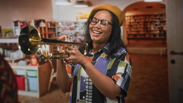 Young woman holding a trumpet with fingers on valves, smiling inside a library building; joyful creativity.